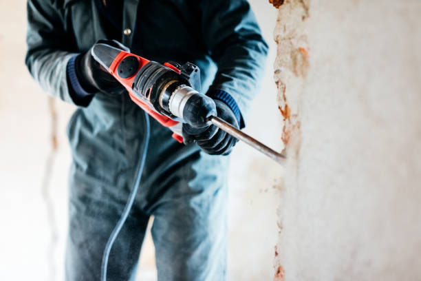 Mature worker demolishing wall with drill at house